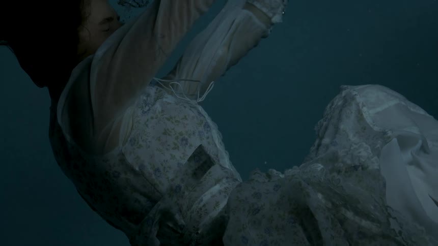 The video is a dark closeup shot of a person floating downwards in deep blue water likely a woman she is wearing a full white or lightcolored dress with lace details that billows around her as she sinks