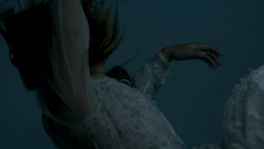 Bubbles rise from a woman sinking through the water in a dress