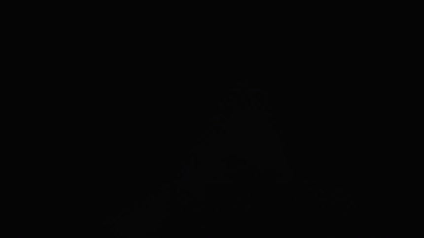 The silhouette of a person jumping while a white light flashes in the background in an allblack environment