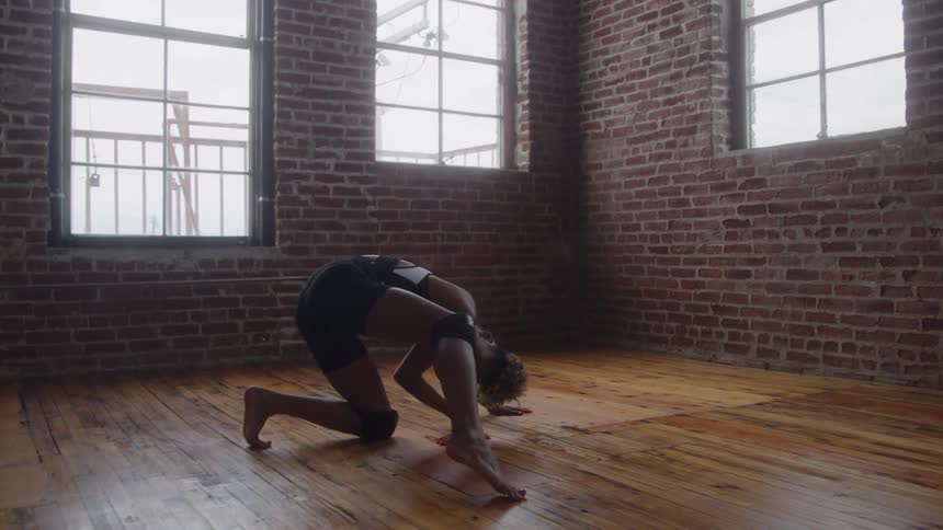 A young woman practices a dance move in an open room with a wooden floor at midday her movements focused and graceful in the natural light