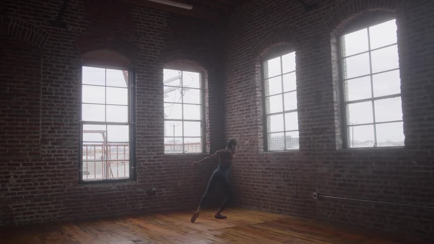 In a rustic brick loft with large windows a lone dancer performs a graceful slow motion routine