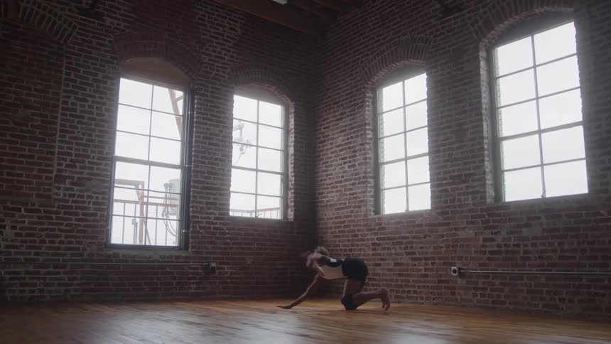 A female dancer practices alone in a dance studio in a brick building