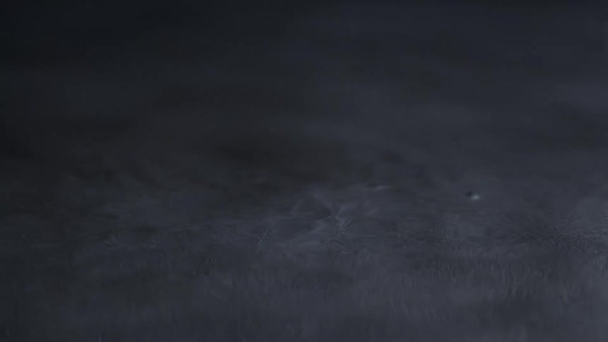 A subtle slow motion dark view shows gentle ripples and movement in a dark gray liquid or muddy water surface with a calm atmosphere