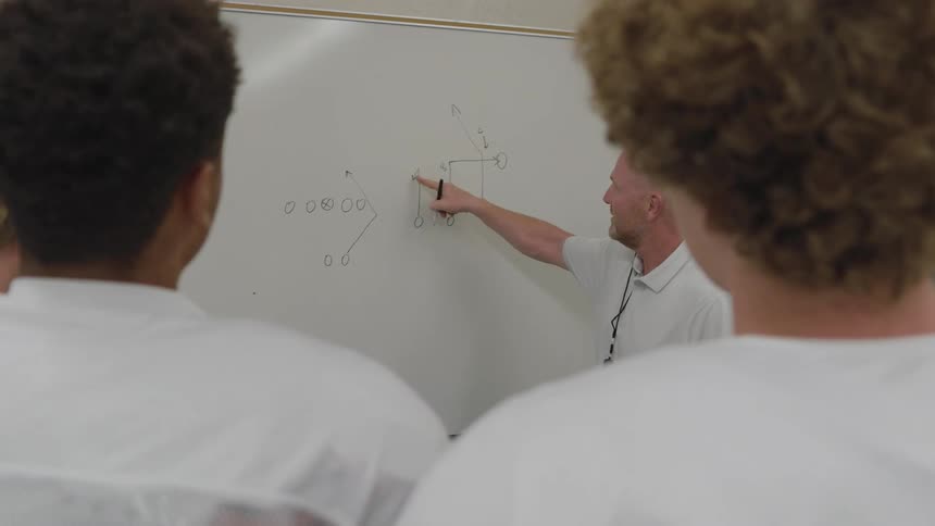 Group watches coach draw sports strategy on whiteboard during instruction