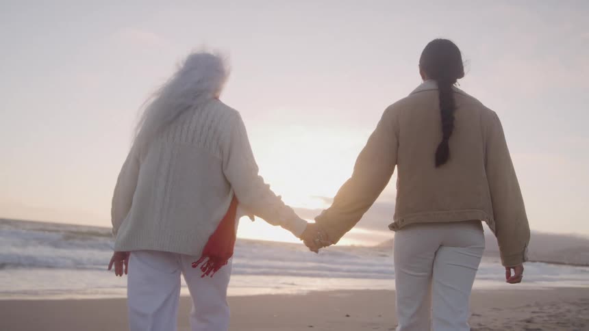 Two women holding hands while walking in the sand