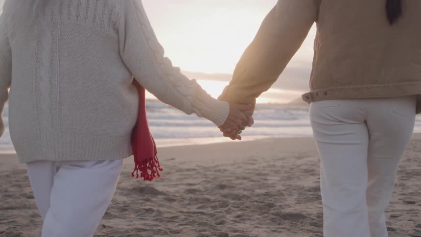 The women hold hands while walking towards the ocean