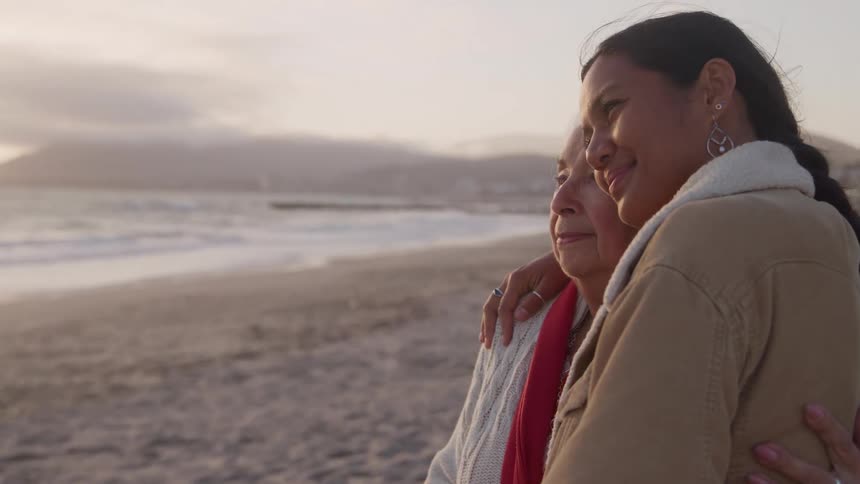 Grandmother and granddaughter smiling and hugging on the beach