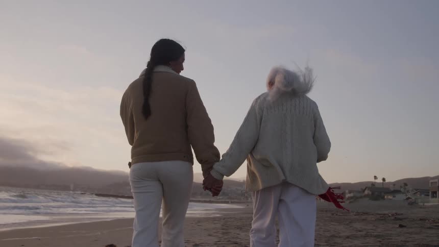 Women hold hands while walking on the beach