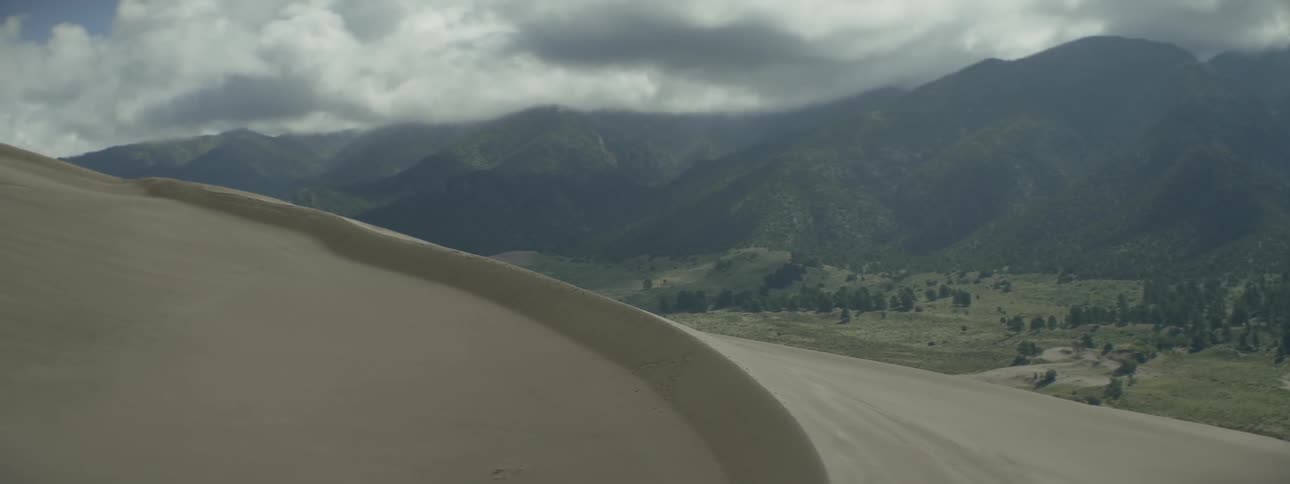 A sand dune leads to mountains ahead