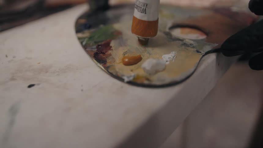 A closeup shows yellow paint being squeezed onto an artists palette