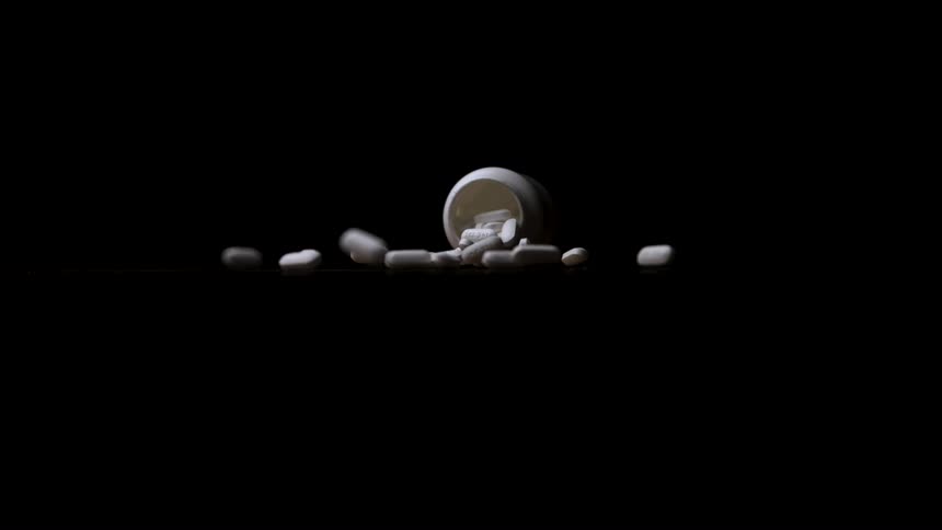Spilled white bottle reveals pills on a dark surface