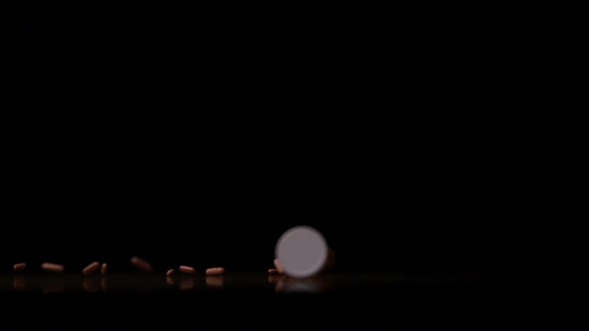White bottle tipped over with brown capsules scattered across dark surface