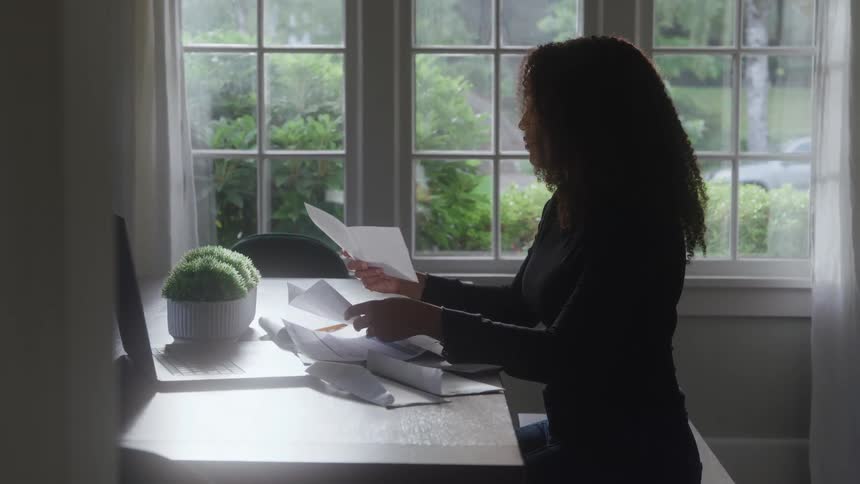 Woman seated at desk reviews documents in front of window overlooking greenery