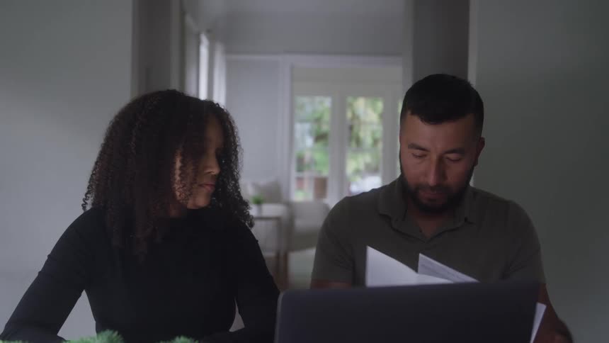 Person presents a document while another reviews it attentively beside a laptop on the table