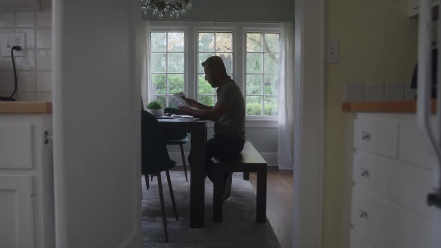 Man seated at table examines papers with natural light streaming through the windows behind