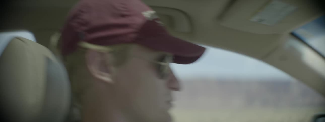 A man adjusts his hat as he drives
