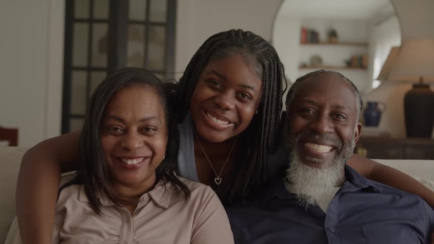 A family of three smiles together on a couch in their living room