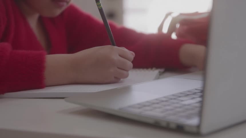 Person writes in notebook with pencil beside a laptop focused in a welllit indoor setting