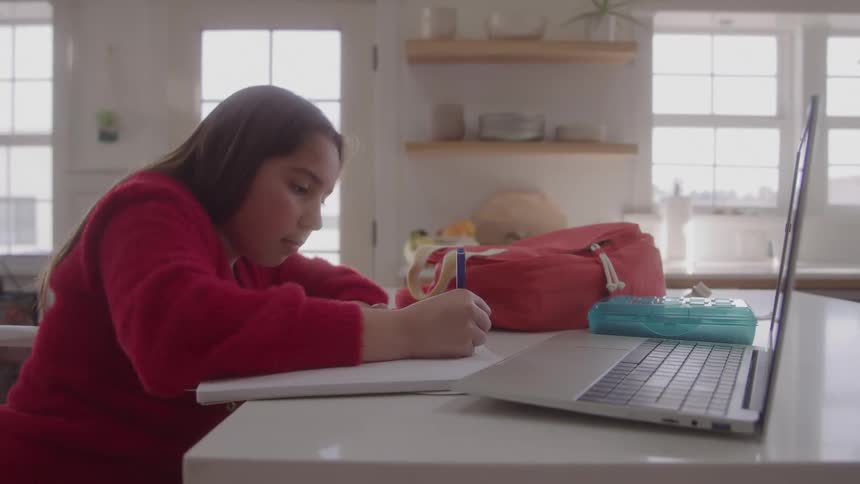 A girl writes with a laptop nearby