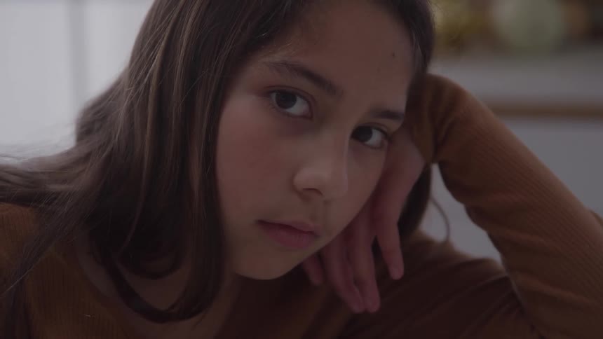 A teenage girl looks bored as she rests her head on her hand