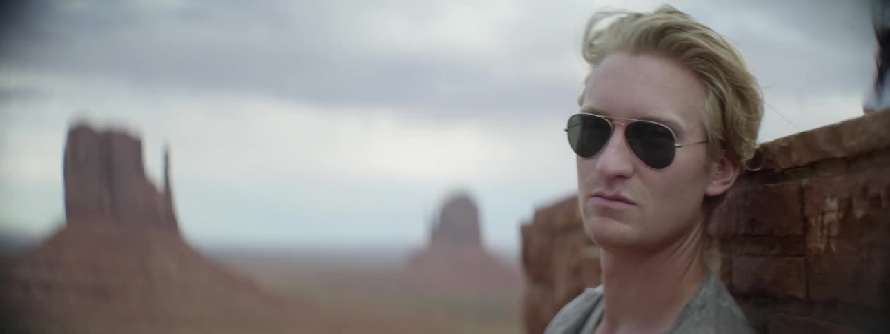 A man wears sunglasses in the desert on a breezy day