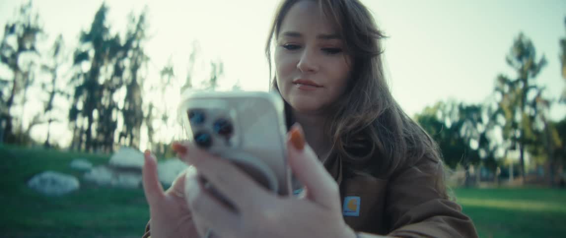 A young woman scrolls on her phone while sitting in a sunny park