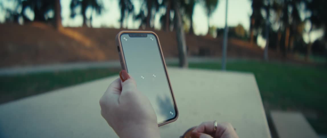 Woman interacts with phone at outdoor table with greenery in the background