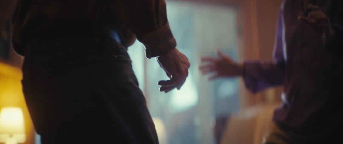 The video is a slightly outoffocus lowlight shot of two people standing close to one another with a bright hazy light source coming from the background creating a silhouetted effect their hands are visible suggesting a conversation or subtle inte