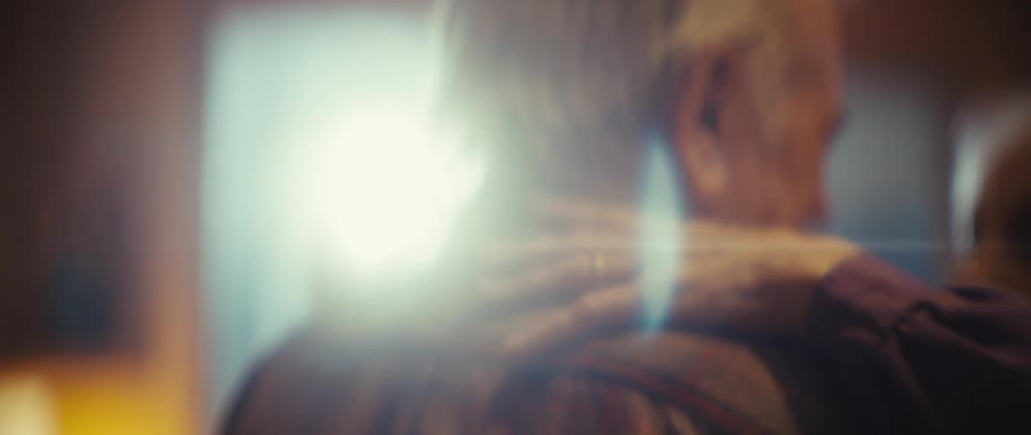 An old woman in a lavender shirt gently touches a mans shoulder as they slow dance in a warm cozy interior the shot focuses closely on the pair highlighting the tender moment shared between them