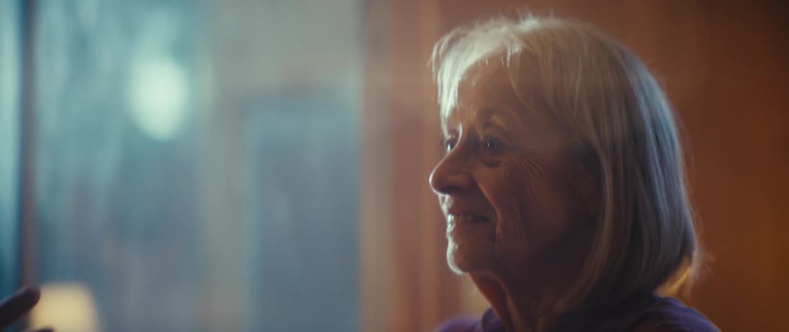 This is a closeup shot of an elderly couple dancing or standing intimately with the man resting his cheek near the womans head and both showing genuine smiles they are bathed in a warm hazy light which highlights their happy and affectionate interac