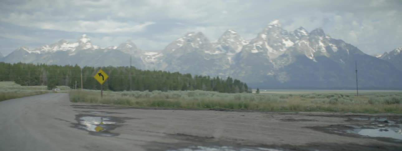 A traffic sign stands next to a road with mountains in the distance