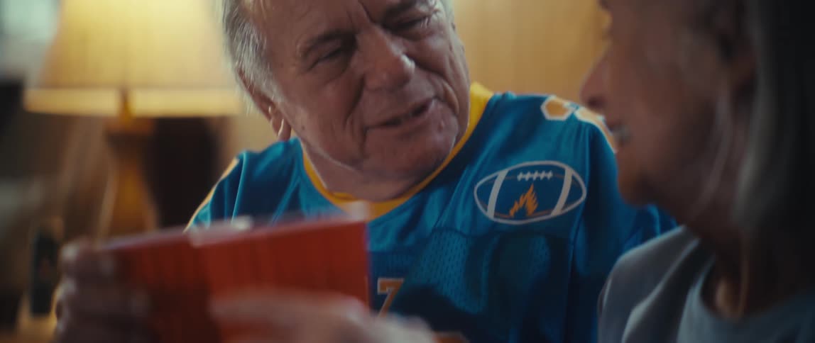 An elderly couple toast each other while drinking from plastic red cups