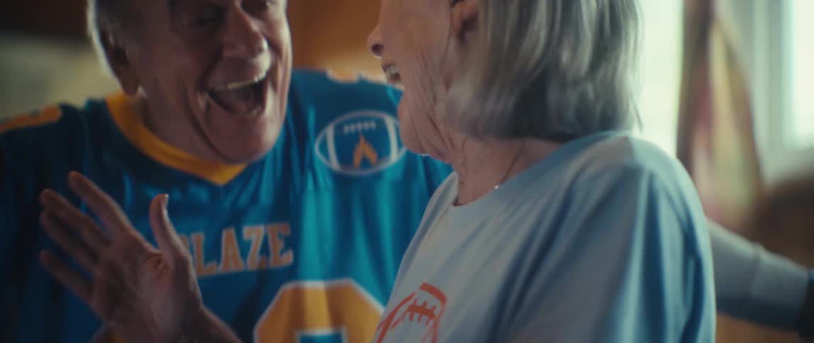An elderly man and woman getting up from the couch celebrating and hugging each other