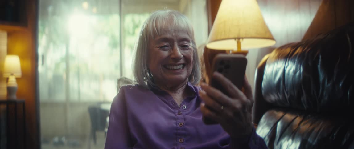 Elderly woman smiling while looking at her smartphone on the couch