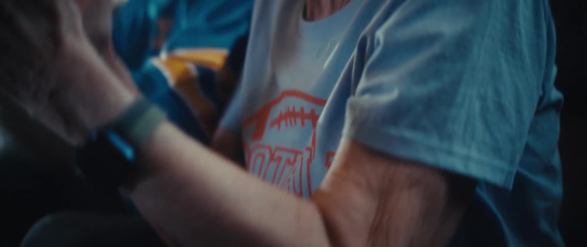 A closeup shot features a person wearing a blue and yellow sports jersey with a watch on their wrist the persons hands are clapping together repeatedly suggesting they are cheering or applauding