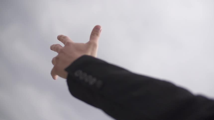 Person raises arm to a cloudy sky