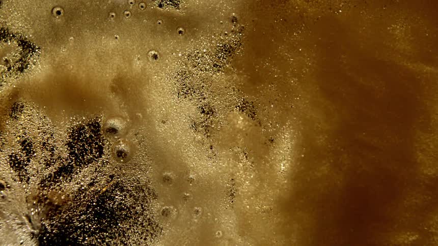 A frothy gold liquid moves and creates bubbles