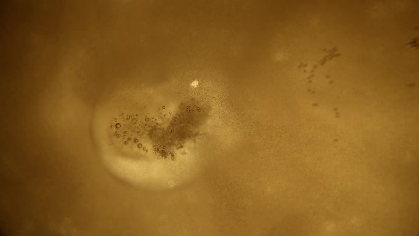 A large bubble pops up in gold liquid and breaks into smaller bubbles