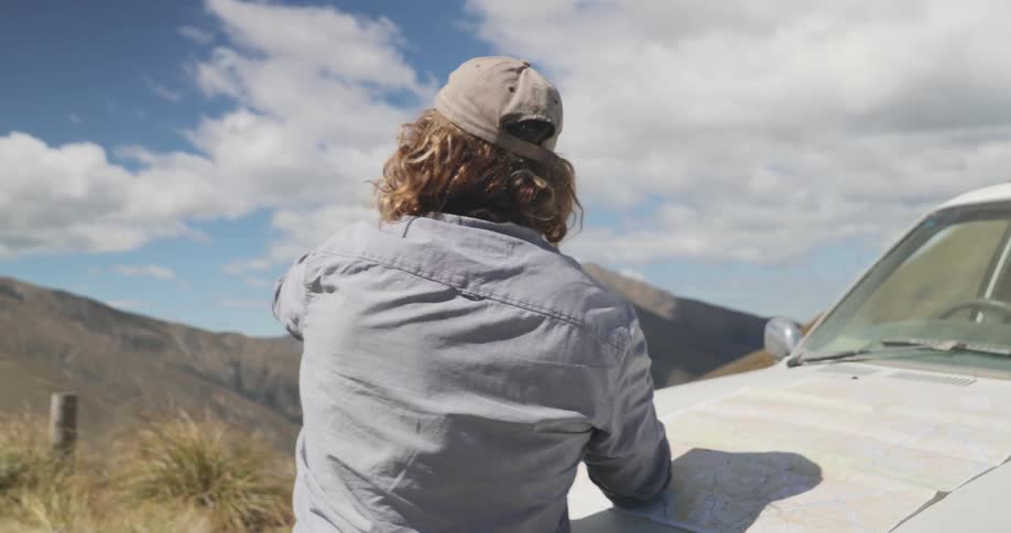 A man is leaning on an old truck and pointing out to the mountains