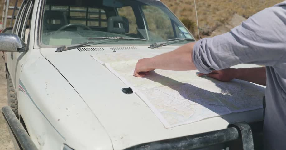 Person examines a map spread out on the hood of an offroad vehicle