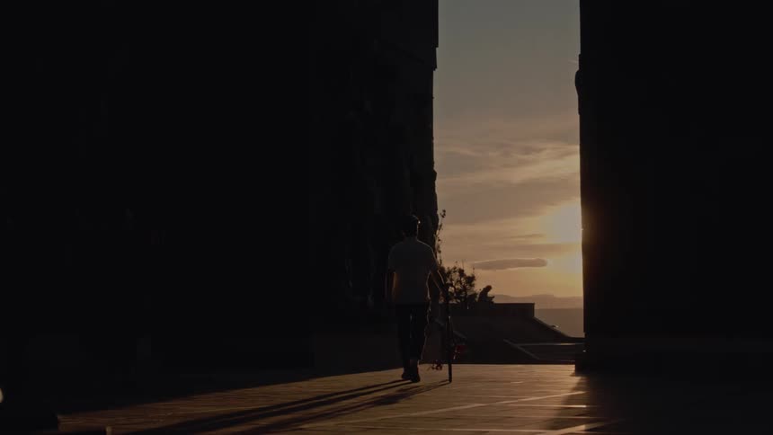 Person walking while pushing a bicycle between buildings at sunset