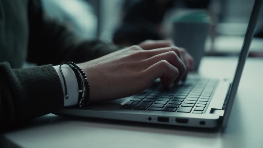 A man is sitting at a desk in an office typing on a laptop