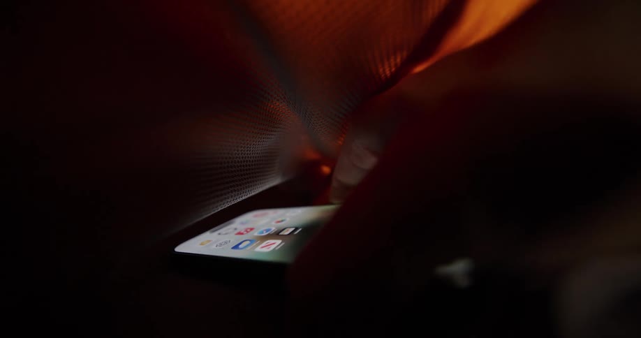 Hand reaching for a smartphone inside a backpack under orange light