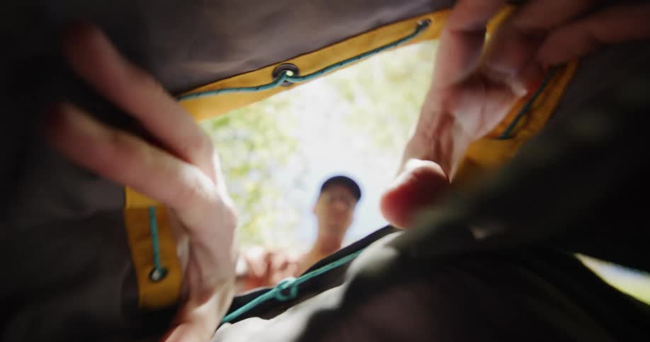 Man wearing dark cap and orange shirt looks into bag with yellow and gray interior in outdoor setting