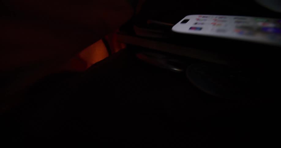 Slow motion closeup shot of a smartphone with its screen on displaying a grid of application icons inside a bag flying around with other items inside the bag