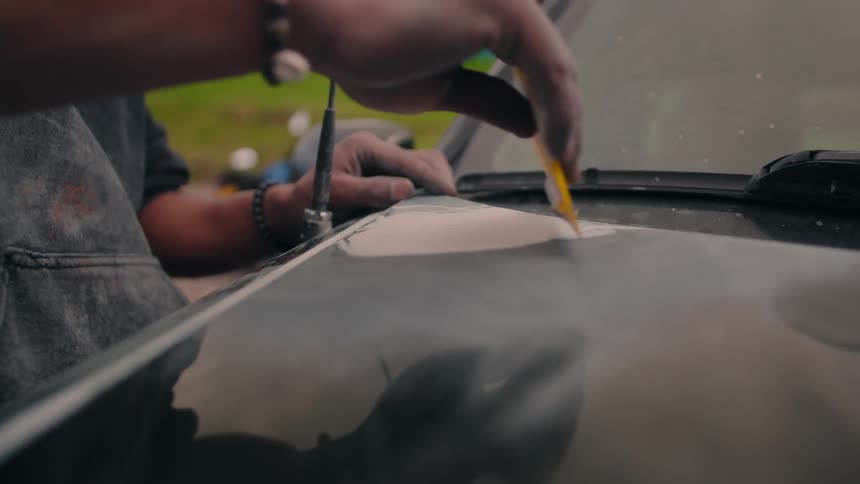Man sands car hood with yellow block as dust gathers on hands in outdoor setting