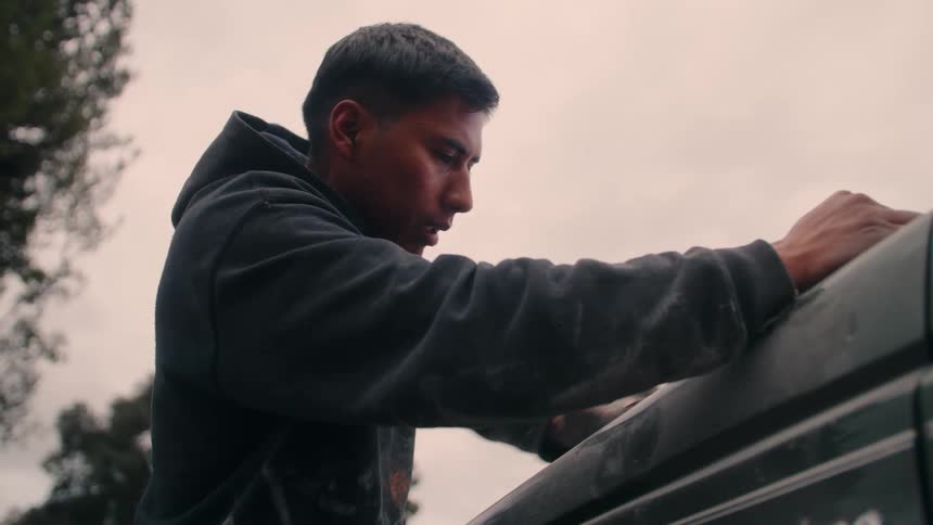 The man leans forward while sanding the car