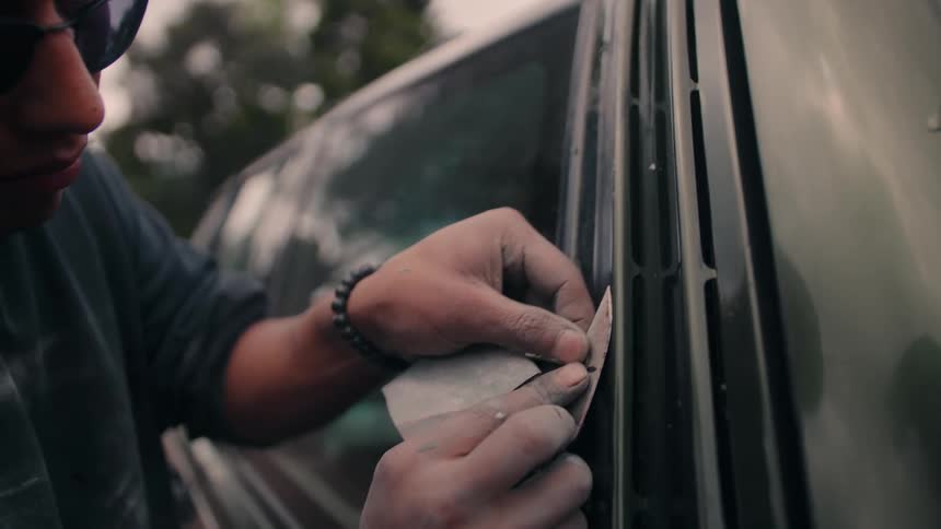 Man adjusts film or seal on dark car window with attention to detail in outdoor setting