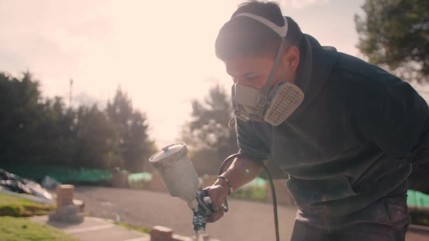 A man wearing a protective mask is using a spraint paint gun