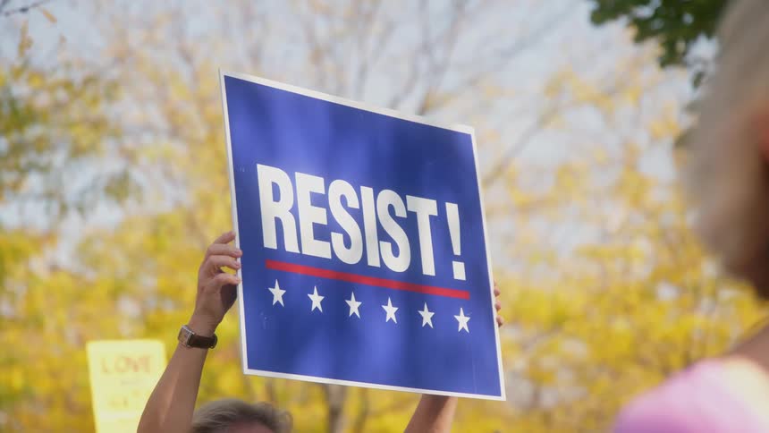 Person holds a protest sign high during a rally on an autumn day